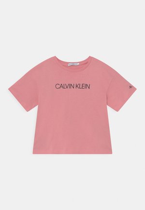 Camiseta de algodón rosa con mangas cortas, cuello redondo y un logo negro de "CALVIN KLEIN" impreso en el frente. Diseño sencillo y holgado.