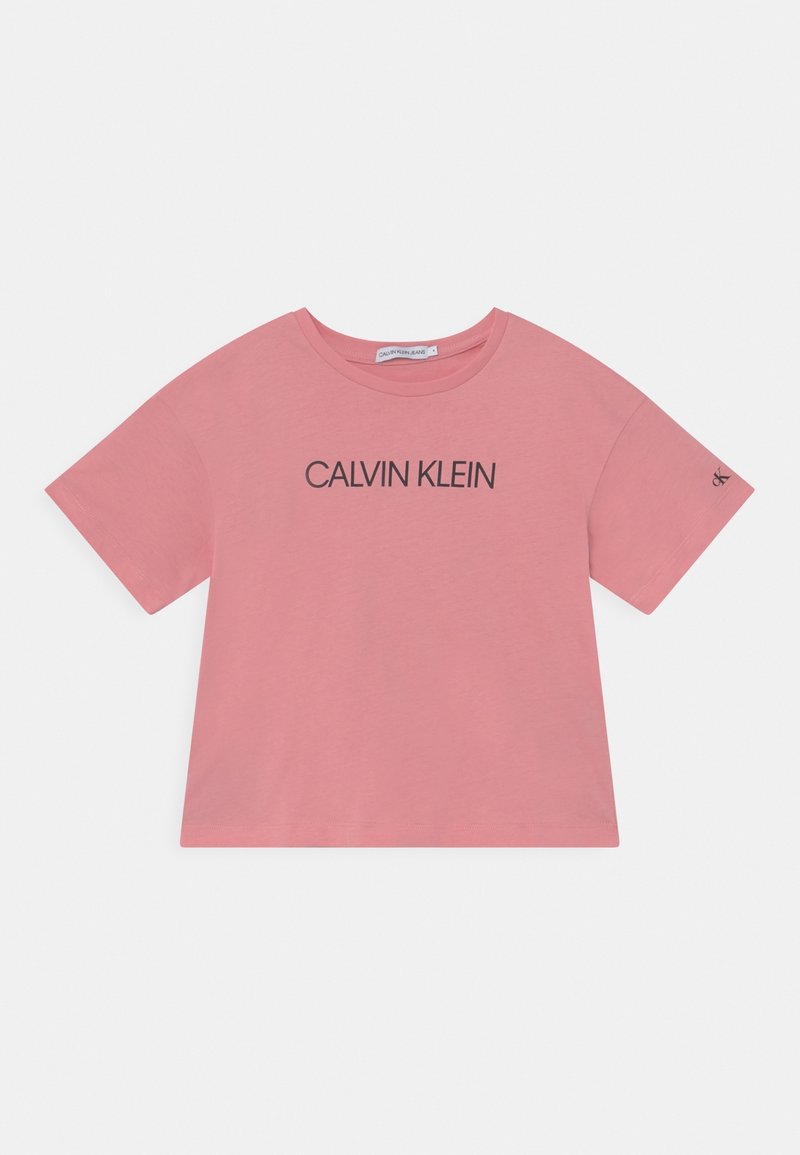 Camiseta de algodón rosa con mangas cortas, cuello redondo y un logo negro de "CALVIN KLEIN" impreso en el frente. Diseño sencillo y holgado.