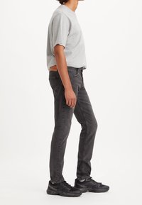 Grå t-shirt och mörkgrå jeans, smal passform, denim-material. Svarta sportskor med strukturerade detaljer. Diskret sömnad synlig på jeansen.