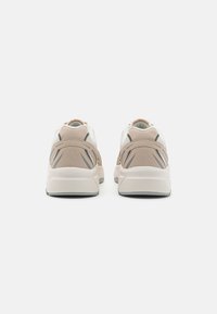 Sneaker mit einem Obermaterial aus beigem und weißem Netz, kontrastierenden grauen Akzenten und einer robusten weißen Sohle. Texturierter Rücken für Grip und Unterstützung.