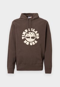 Brūns kapuces džemperis ar priekšējām kabatām, regulējams kapuces aukla un balts Timberland NH USA logo ar koku grafiku uz krūtīm.