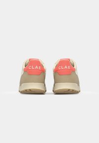 Beige sneakers with a textured upper and pink heel accents. Features a logo on the back and a cushioned sole for comfort.