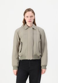 Kaki bomber jakna, s patentnim zatvaračem sprijeda, rebrasti manšeti i rub, dva bočna džepa, glatka tkanina, minimalistički dizajn, s ravnim ovratnikom.