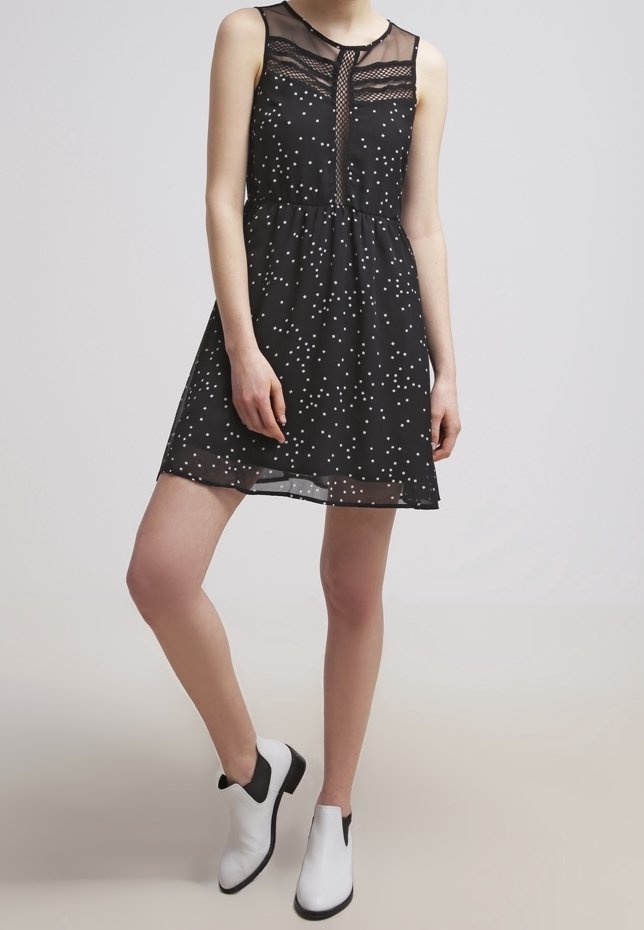 Robe noire à pois blancs, décolleté transparent, sans manches, forme évasée. Associée à des bottines noires et blanches.