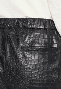 Zwarte leren broeken met een textuur in krokodillenprint. De tailleband is elastisch en er is één achterzak.