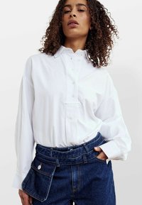 Hvid langærmet skjorte med knap-ned krave, med en frontlomme og afslappet pasform, parret med mørke denim højtaljede bukser.