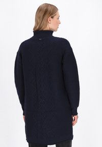 Granatowy, oversize sweter wykonany z dzianiny, z wysokim kołnierzem, z teksturowanym wzorem w zygzaki na plecach oraz prążkowanymi rękawami dla dodatkowego efektu.