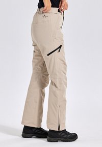 Beige outdoor broek met ritszakken, rechte snit, gemaakt van lichte stof, met een taps toelopende pijp en zwarte hardware accenten.