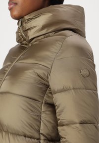 Olijfgroene pufferjack met capuchon, voorzien van een ritssluiting, gestikte textuur en een logo-patch op de linker schouder.
