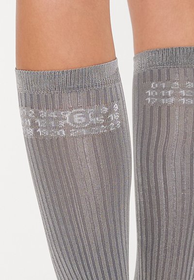 Knee-high hallid mustas, millel on ribitud tekstuur ja dekoratiivne mustriga riba üleval. Pehme, opak materjal kerge läikega.
