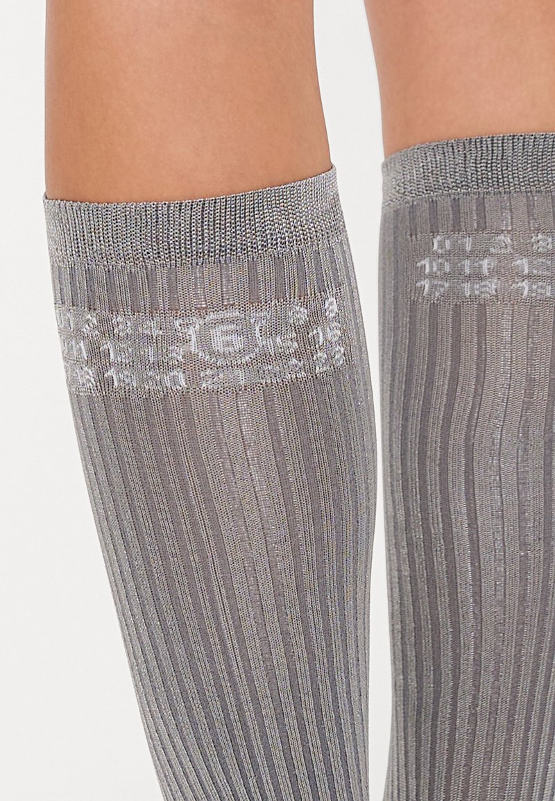 Chaussettes montantes grises avec une texture côtelée et une bande décorative à motifs en haut. Matière douce et opaque avec un léger éclat.