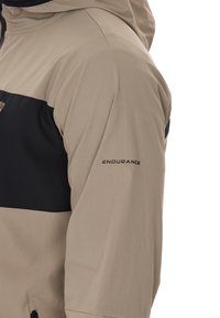 Beige- und schwarze Jacke mit strukturiertem Stoff, einer Kapuze und dem Wort "ENDURANCE", das auf dem Ärmel gedruckt ist.