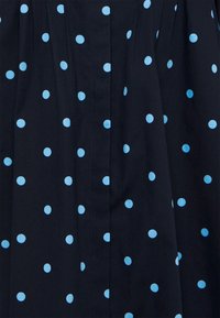 Marinblått tyg med ljusblåa prickar, med en plisserad design. Slät textur med jämnt fördelade mönster över ytan.