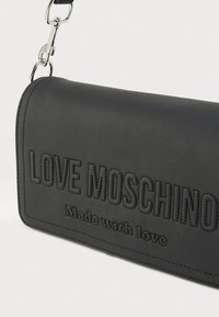 Μαύρο δερμάτινο πορτοφόλι clutch με ανάγλυφη επιγραφή "LOVE MOSCHINO" και το κείμενο "Made with love", με ασημένια αλυσίδα και λεία υφή.