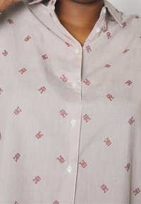 Camicia button-up con motivo a righe in colori chiari e un motivo geometrico rosso. Bottoni bianchi e design del colletto classico.