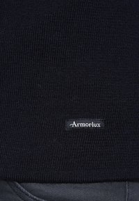 Tissu tricoté côtelé bleu marine avec une petite étiquette noire comportant le texte blanc "ArmorLux" en bas. Texture lisse avec un motif serré.