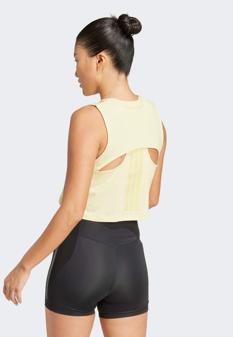 Top corto amarillo claro con cortes en la espalda, que presenta tres franjas verticales. Pantalones cortos ajustados negros con cintura alta. Textura suave.