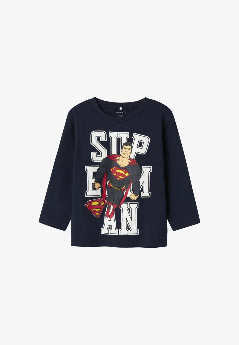 T-shirt à manches longues bleu marine présentant un grand graphisme de Superman, avec du texte blanc indiquant "SUPERMAN" et des accents rouges sur le logo et la cape.