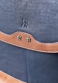 Leather bag featuring a navy main section and a tan accent band with floral studs. Textured finish and contrasting stitching details.