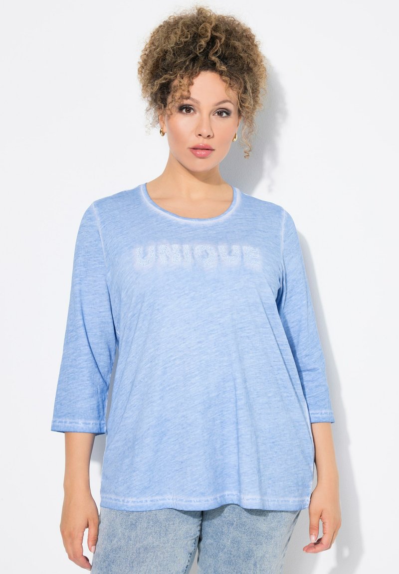 Světle modrý dlouhý rukáv s kulatým výstřihem a textem "UNIQUE" v mírně vyvýšeném designu. Vyrobeno z měkké, texturované tkaniny.