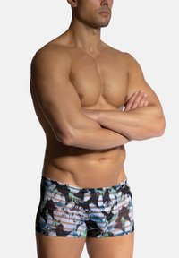 Simshorts i ett flerfärgat kamouflage-mönster som har svart, vitt och nyanser av grönt, med en åtsittande design och elastisk midja.