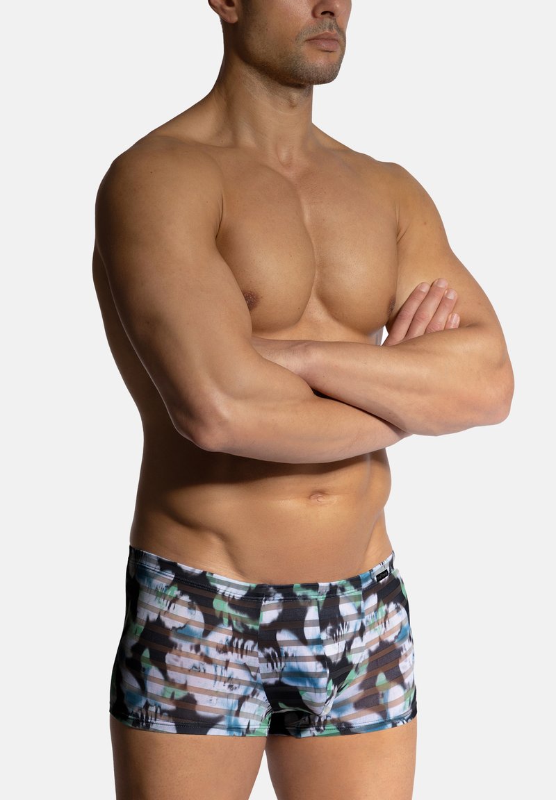 Simshorts i ett flerfärgat kamouflage-mönster som har svart, vitt och nyanser av grönt, med en åtsittande design och elastisk midja.