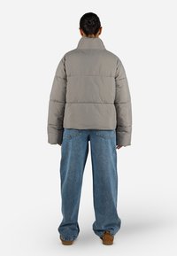 Grå pufferjakke med høy krage og oversized passform, med horisontalt quiltet design og ribbestrikkede mansjetter, paired med vide blå jeans.