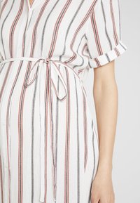 Vestido branco de botão, com riscas verticais pretas e vermelhas, apresentando mangas enroladas e cinto amarrado na cintura. Tecido suave e texturizado.