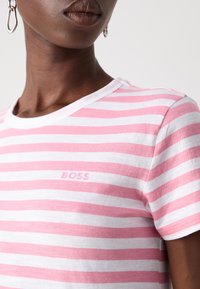Rosa og hvit stripete T-skjorte laget av bomull, med rund hals, korte ermer og en subtil "BOSS"-logo på brystet.