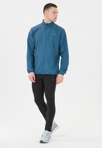 Lichte blauwe jack met hoge kraag en ritssluiting, gecombineerd met zwarte aansluitende broeken en grijze hardloopschoenen. Eenvoudig ontwerp, gladde textuur.