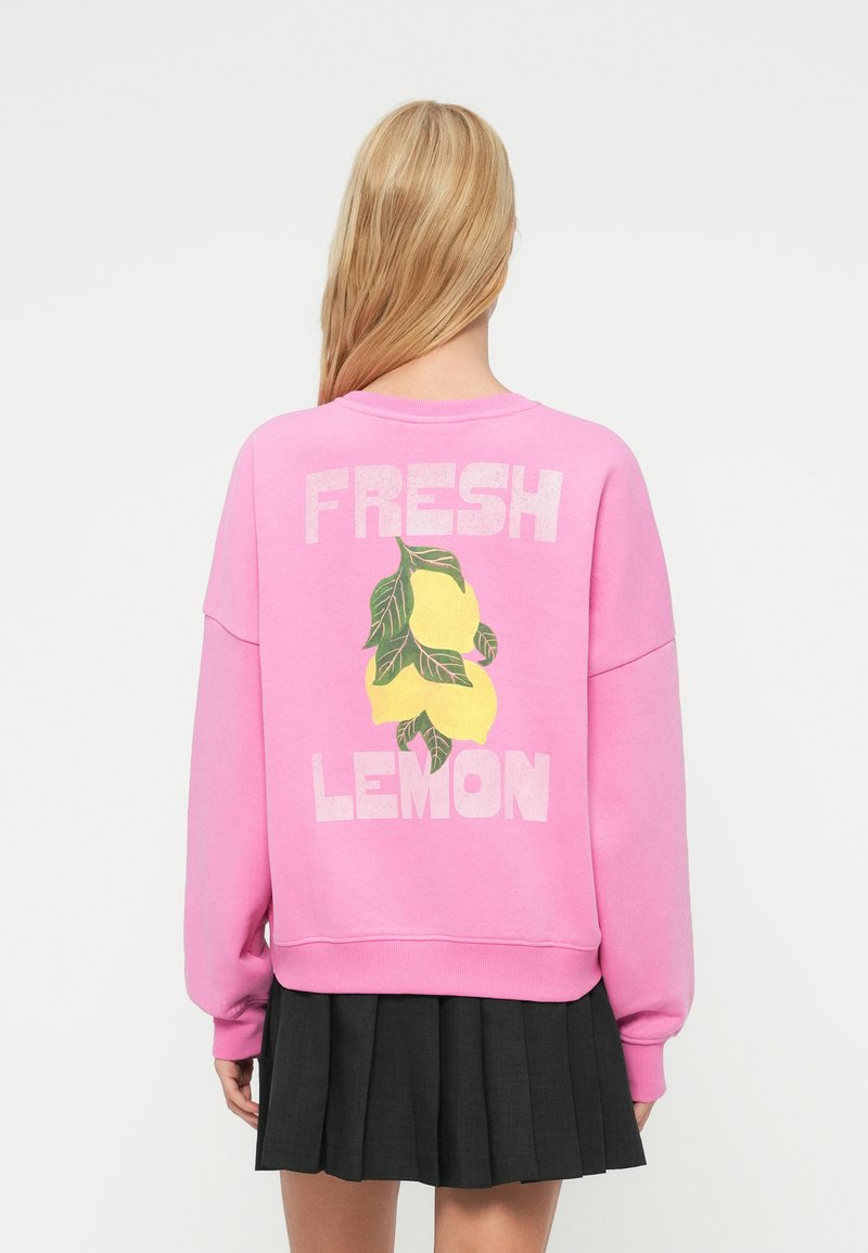 Ροζ φούτερ με το κείμενο "FRESH LEMON" και κίτρινες γραφικές εικόνες λεμονιού στην πλάτη· κατασκευασμένο από απαλό υλικό με άνετη εφαρμογή και ριμπ μανσέτες.