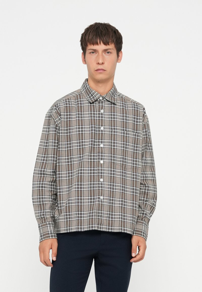 Brown checkered shirt with white and black lines, button-down collar, long sleeves, and a front pocket, made of soft fabric.