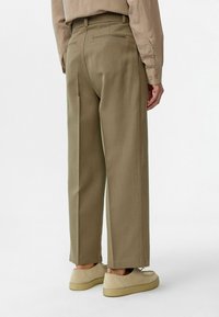 Khaki broek met rechte pijpen, achterzakken, een getailleerd ontwerp en een textiel met structuur. Draag het met lichtgekleurde schoenen.