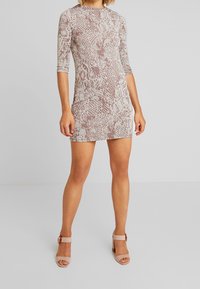 Käärmeennahkakuosiset minimekot, joissa on pitkät hihat, vaaleanpunaiset ja beiget värit, istuva malli ja pehmeä, sileä rakenne, yhdistettynä nude-värisiin korkokenkiin.