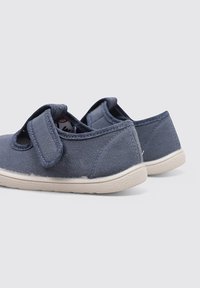 Zapatillas de lona azul marino con una correa de velcro, suela de goma crema y textura suave. Diseñadas para la comodidad y facilidad de uso.
