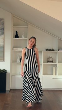 Black and white striped dress with a fitted bodice and flared skirt, made of smooth fabric. Model stands barefoot in an indoor setting.