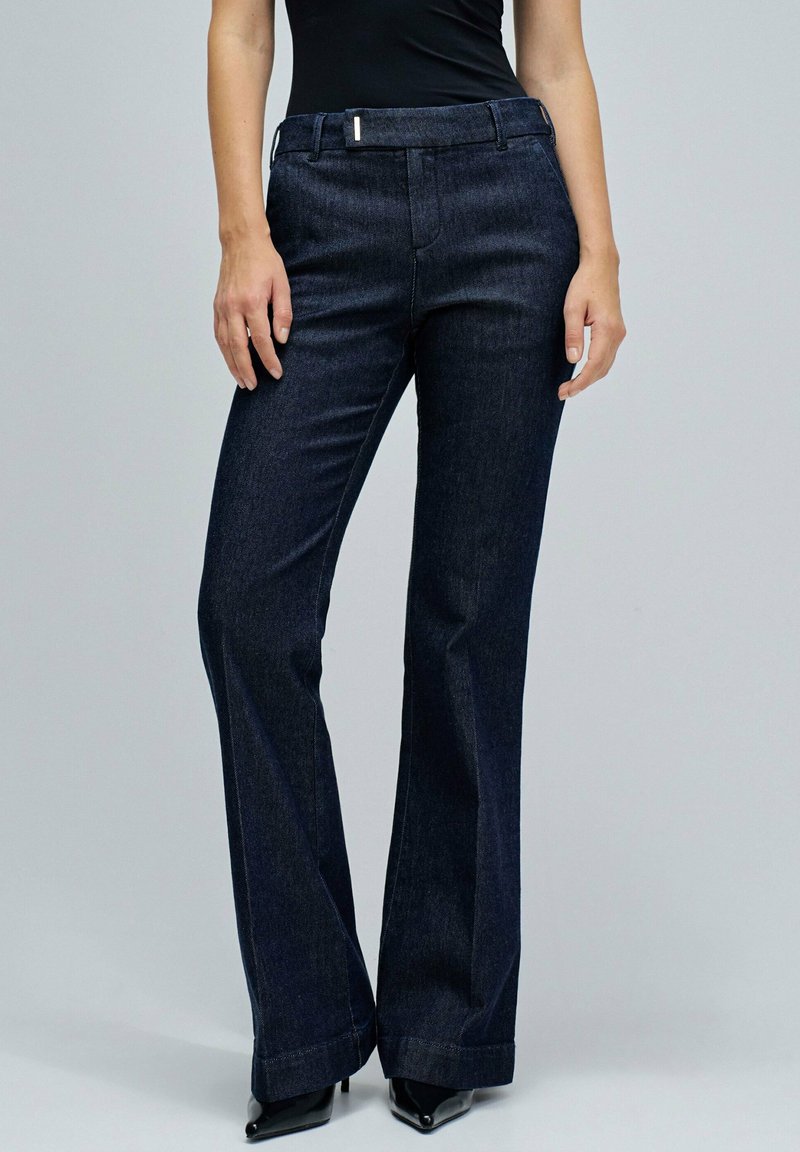 Jeans acampanados de color azul oscuro, confeccionados en denim, con un diseño clásico de cinco bolsillos y un cierre de botón en la cintura, con una textura suave.