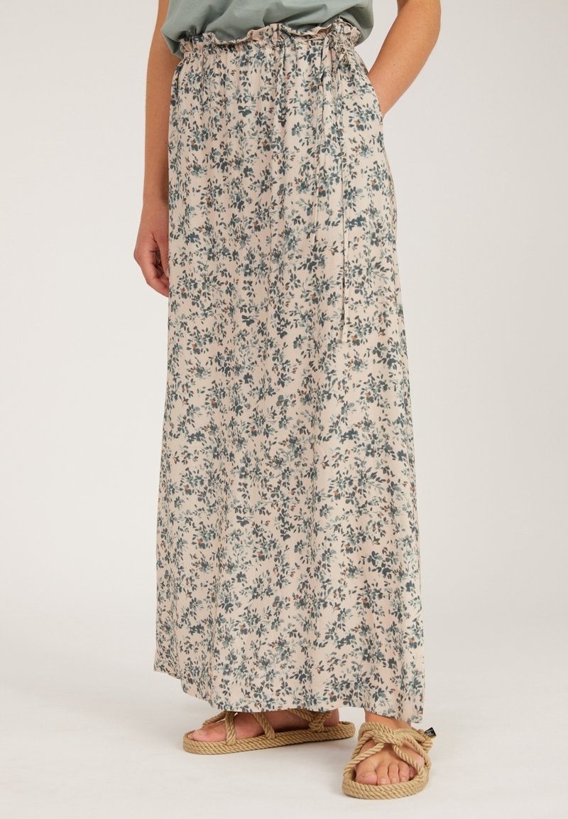 Jupe longue beige avec petit imprimé floral vert, taille élastique froncée avec lien, portée avec un haut vert clair et des sandales en corde couleur tan.