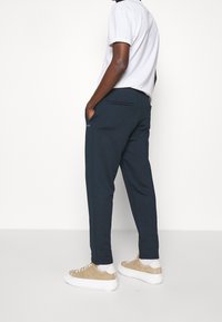 Dunkelblaue Sweatpants mit schmalem Schnitt, Seitentaschen und einer Gesäßtasche. Kombiniert mit einem einfachen weißen T-Shirt und beigen Sneakers.