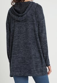 Mörkgrå hoodie med luva, som har ett strukturerat tyg, lös passform och långa ärmar. Sömlös design med ribbad huva.