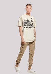 Beige t-shirt with a black graphic print of waves and Japanese text, paired with beige cargo pants and white sneakers. Casual fit.