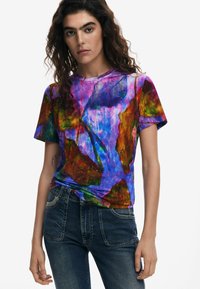 T-shirt di cotone colorato con motivi di foglie astratte in viola, verde e rosso. Maniche corte, collo rotondo, vestibilità rilassata.