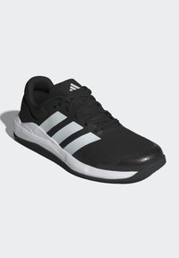Chaussure de sport noire avec une tige en mesh, trois rayures blanches sur le côté et une semelle en caoutchouc texturée avec un capuchon de toe lisse.
