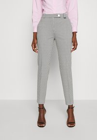Pantaloni a righe grigie e bianche con una vestibilità su misura, dotati di passanti per cintura e orlo accorciato. Complementati da sandali neri con cinturini.