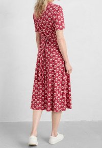 Rotes, kurzärmliges Kleid mit Blumenmuster, tailliert und hinten gebunden, aus weichem Material, knielanger Rock, kombiniert mit weißen Sneakers.