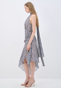 Robe à carreaux bleus et blancs avec un col halter, un corsage froncé et un ourlet asymétrique, associée à des sandales à talons beiges.