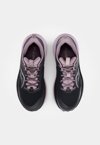 Zapatillas de trail running en negro y púrpura claro, con tejido de malla, cordones texturizados y una suela acolchada. Presentan el logo de la marca en el lateral.