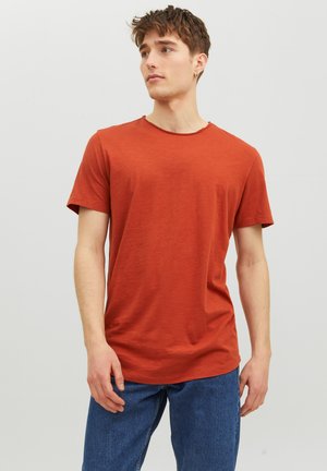 Rostfarbendes Kurzarm-T-Shirt mit rundem Ausschnitt. Hergestellt aus einem weichen, texturierten Stoff. Getragen mit blauen Denim-Jeans.