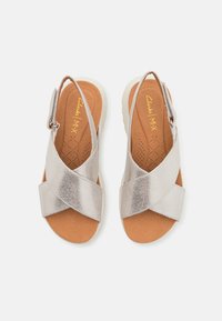 Zilverkleurige metalen sandalen met kruisbanden, gevoerde binnenzool en een witte rubberen zool. Verstelbare enkelband voor een goede pasvorm en comfort.