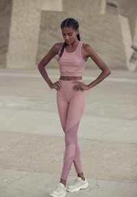Light pink athletic crop top and leggings with textured accents, paired with white chunky sneakers, set against a neutral background.